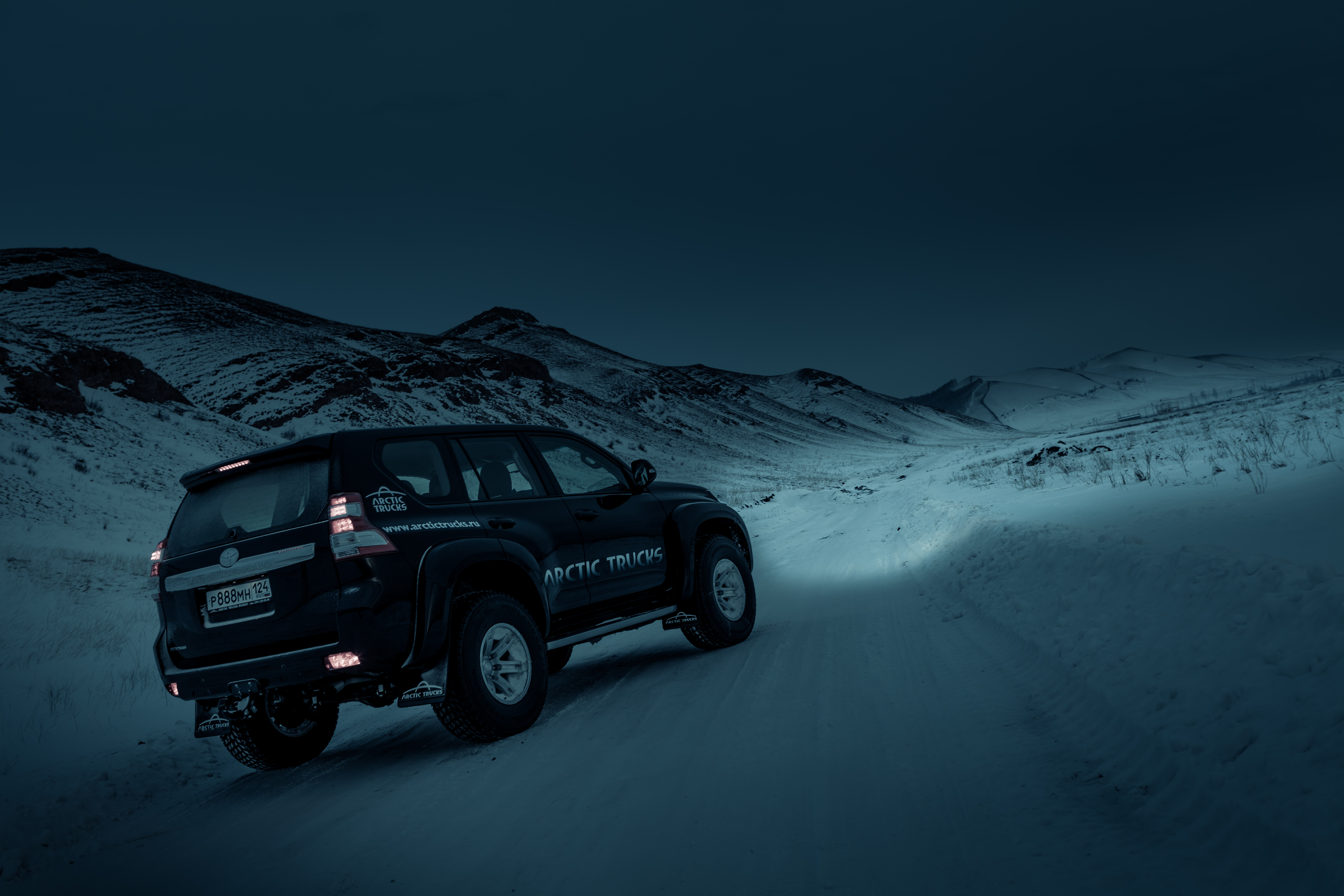 Off-road SUV drives on a snow-covered mountain road under a dim, overcast sky, conveying a sense of adventure and solitude in the wilderness.